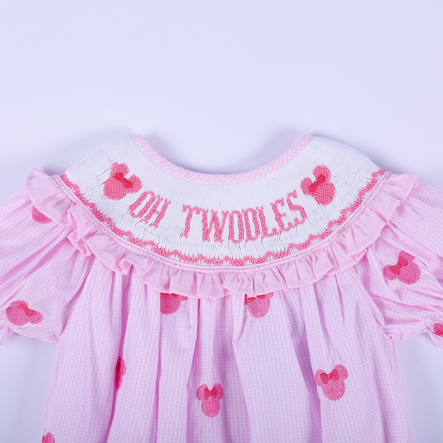 Close-up of hand smocked pink neckline featuring embroidered Oh Twoodles lettering and pink mouse silhouette.