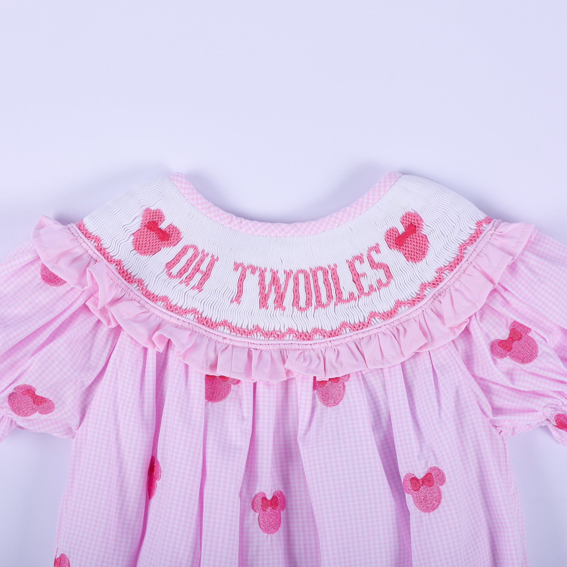 Close-up of hand smocked pink neckline featuring embroidered Oh Twoodles lettering and pink mouse silhouette.