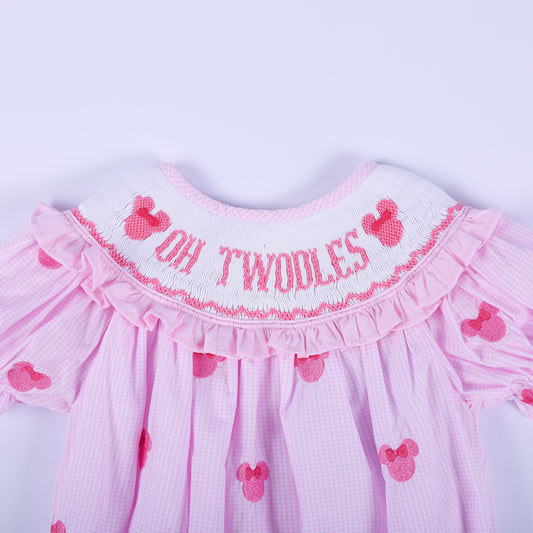 Close-up of hand smocked pink neckline featuring embroidered Oh Twoodles lettering and pink mouse silhouette.