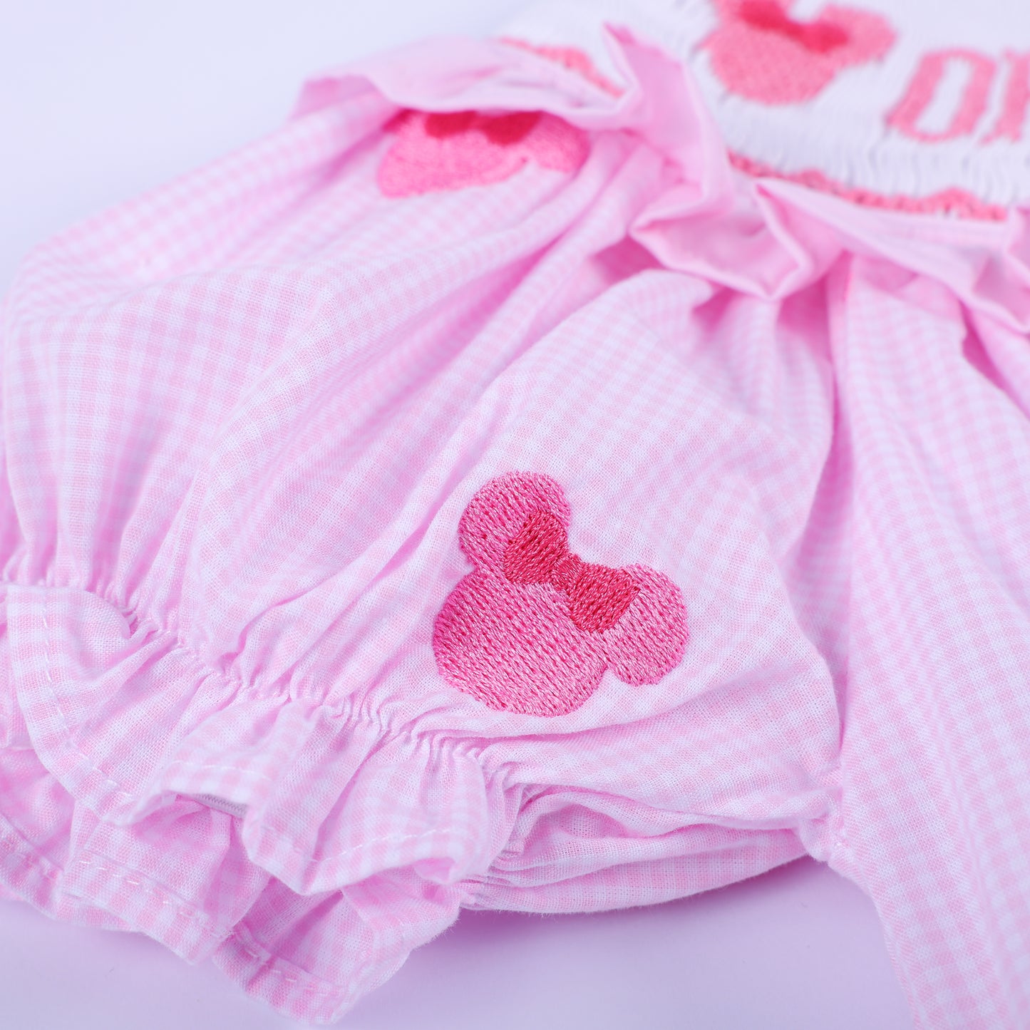 Detailed view of elastic ruffled leg opening and embroidered mouse head on pink gingham hand smocked bubble.