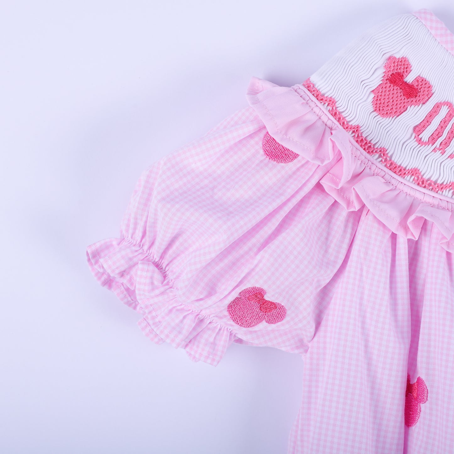 Close-up shot of pink gingham flutter sleeve with ruffled cuff and hand embroidered mouse head on baby bubble.