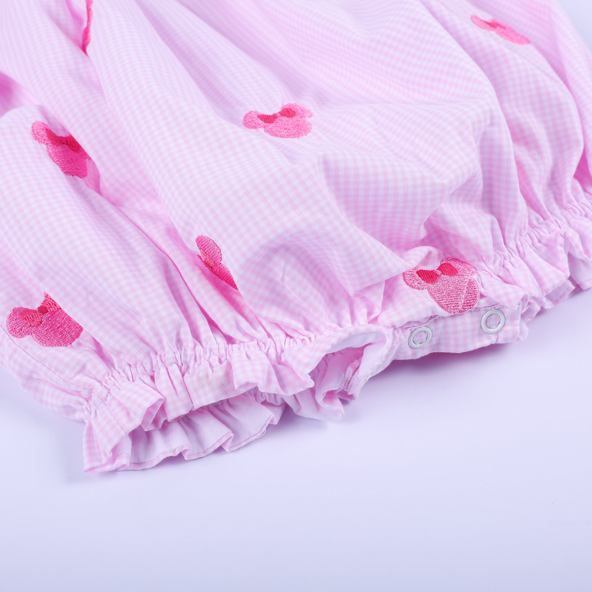 Close-up of bottom snap closure and elastic ruffled hem on pink gingham Oh Twoodles hand smocked bubble romper.