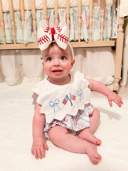 Baby girl sitting in Patriotic Grandmillennial embroidered bubble with scalloped collar and American flag bows.