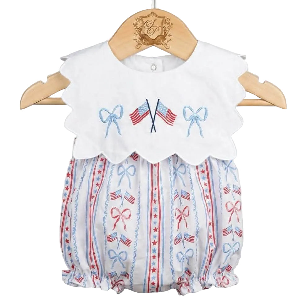 Patriotic Grandmillennial embroidered baby bubble on wooden hanger featuring scalloped collar with flag embroidery.