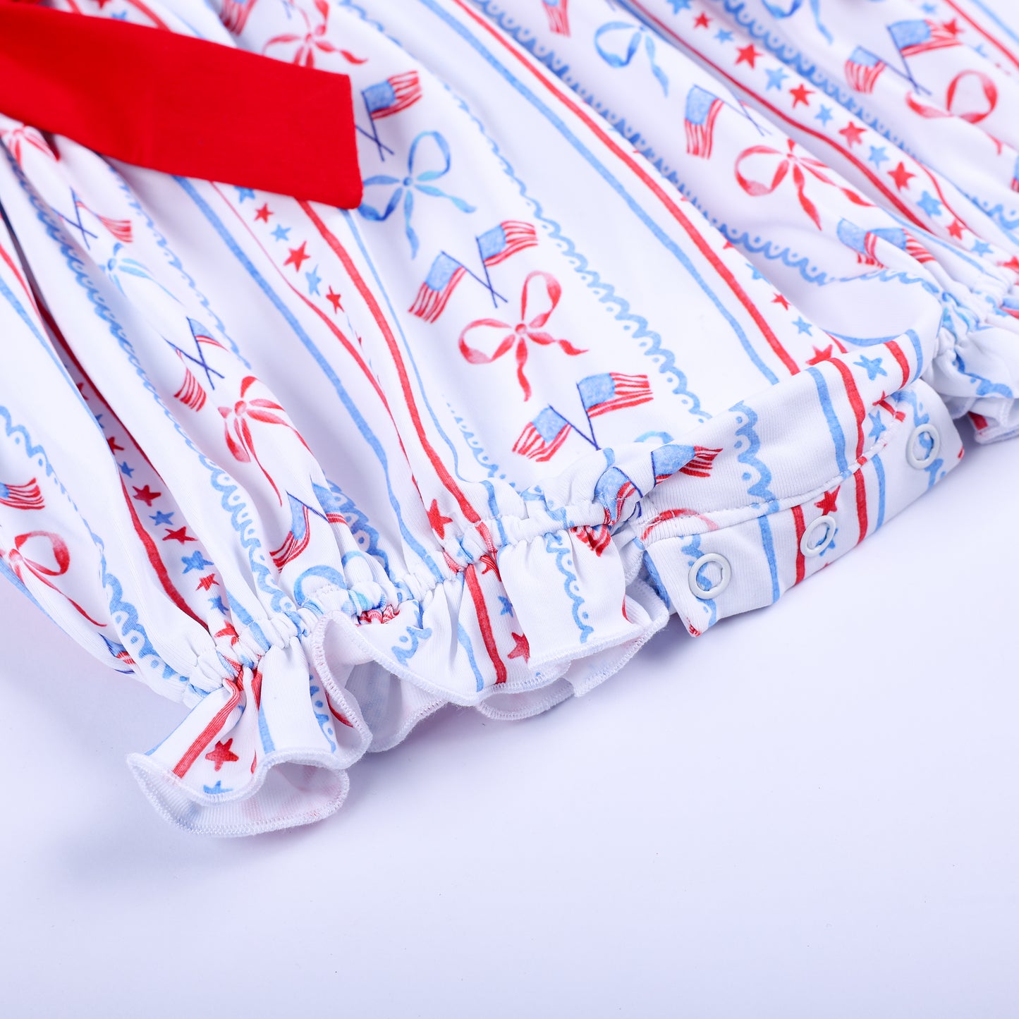 Detailed close-up of ruffle leg openings and convenient snap closure on hand smocked patriotic baby bubble outfit.