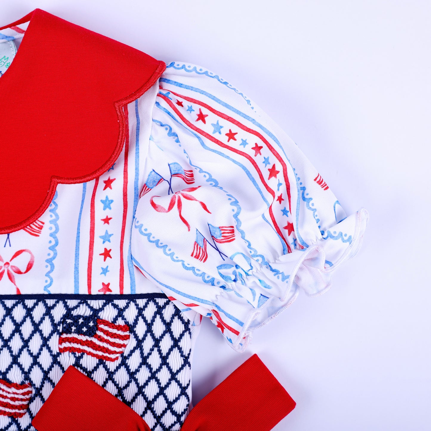 Close up view of puffy elastic sleeve and red scalloped collar on America the Beautiful patriotic baby top set.