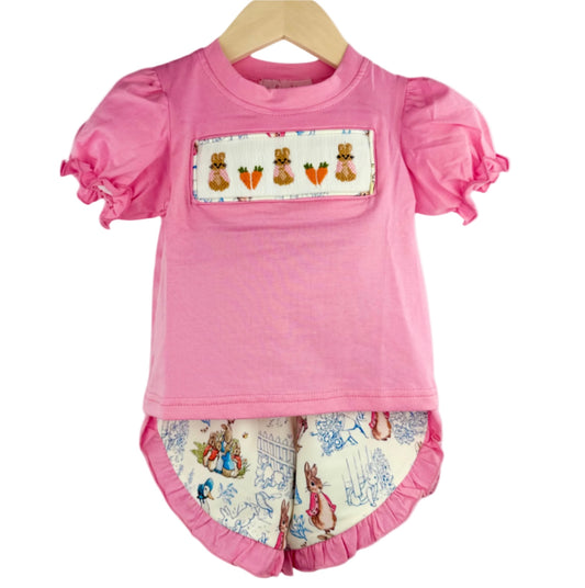 Pink hand smocked girls top with Peter Rabbit and carrots design, and matching Peter Rabbit print bloomers set on a hanger.