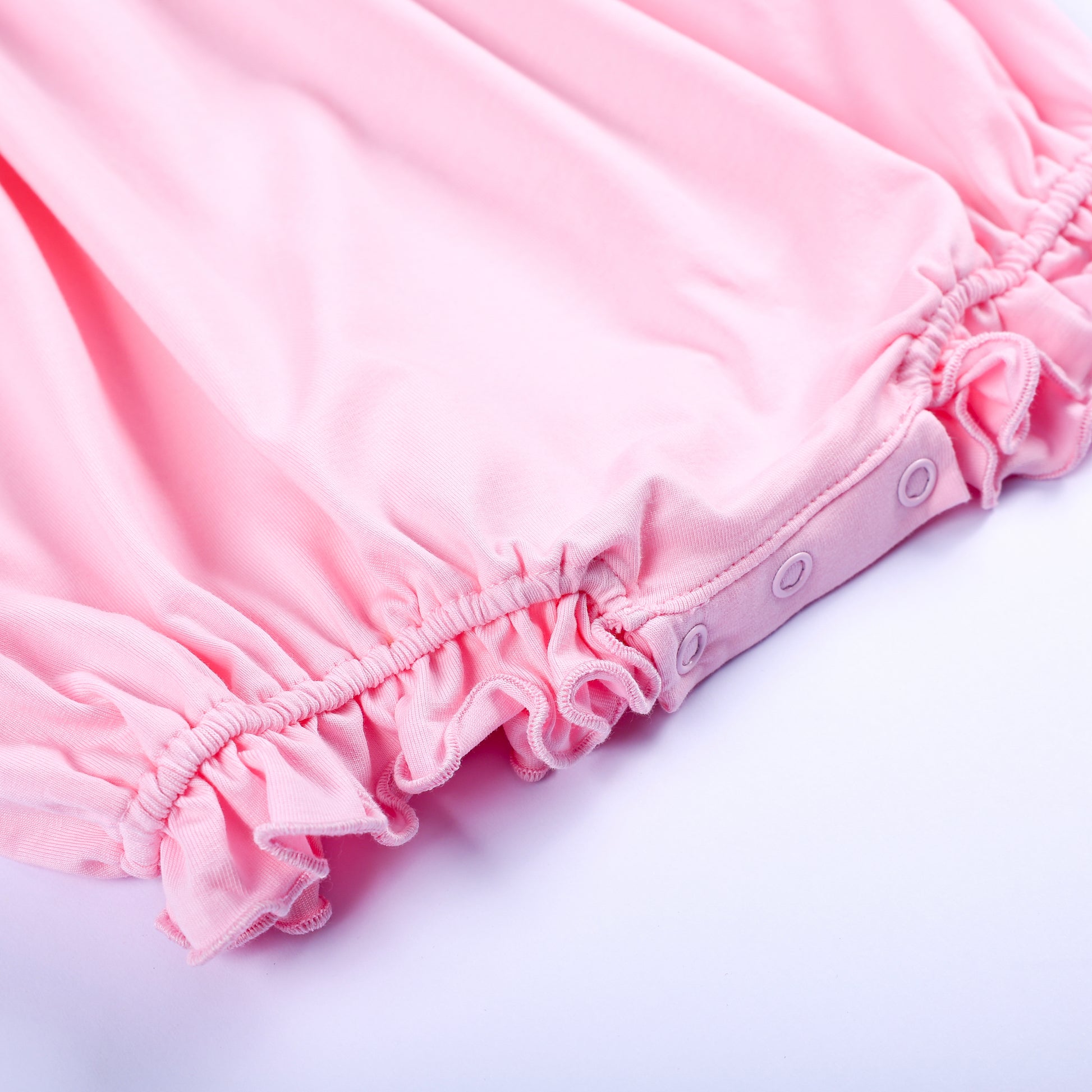 Detailed shot of convenient bottom snap closures and ruffled trim on a pink baby girl embroidered bubble romper.