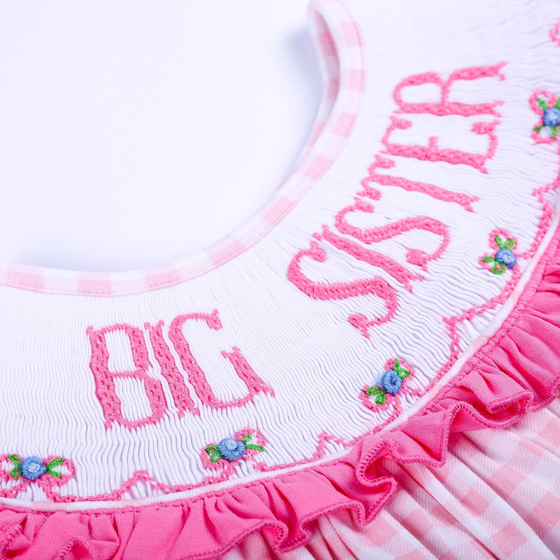 Detailed close-up of intricate hand-embroidered Big Sister lettering and smocking on a pink ruffled collar.