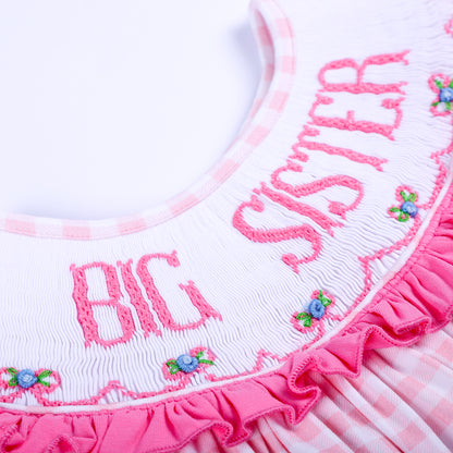 Detailed close-up of intricate hand-embroidered Big Sister lettering and smocking on a pink ruffled collar.