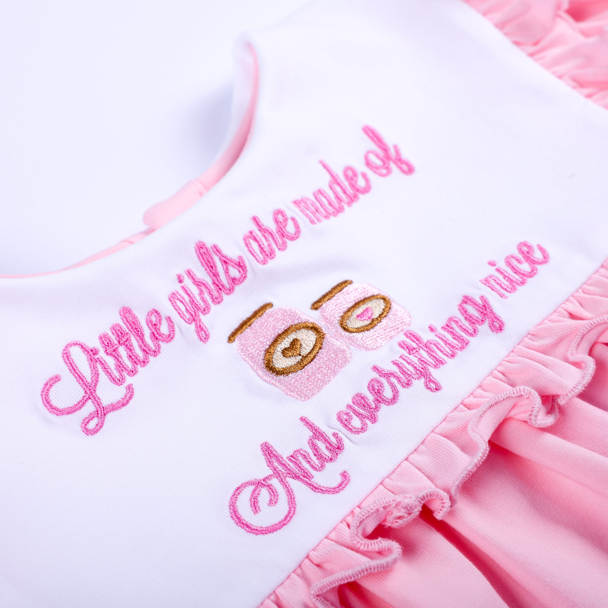 Close-up macro view of pink cursive embroidery quote and cute spice jar designs on white boutique baby collar.