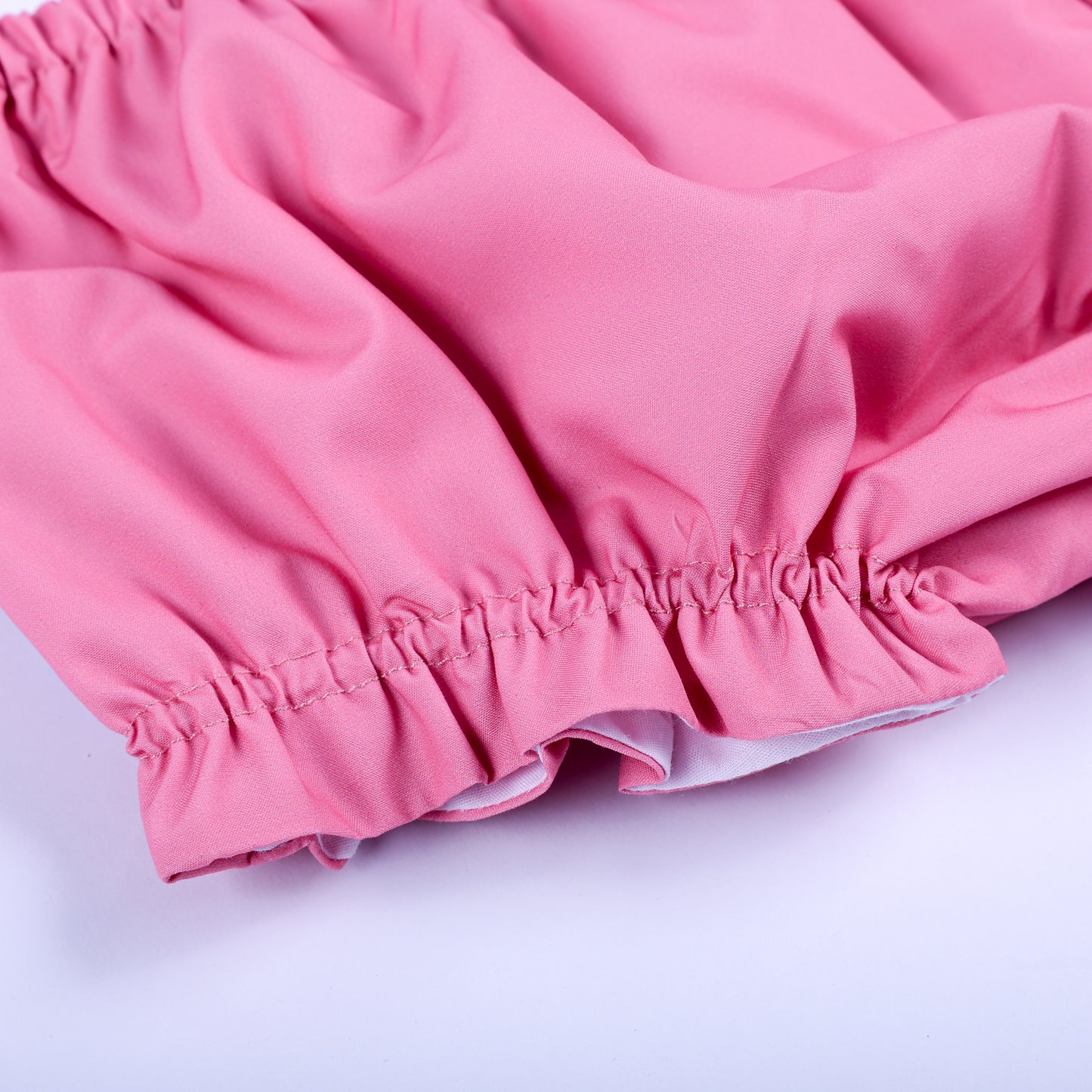Detail view of ruffled elastic leg opening on soft solid pink diaper cover bloomer for baby girl outfits.