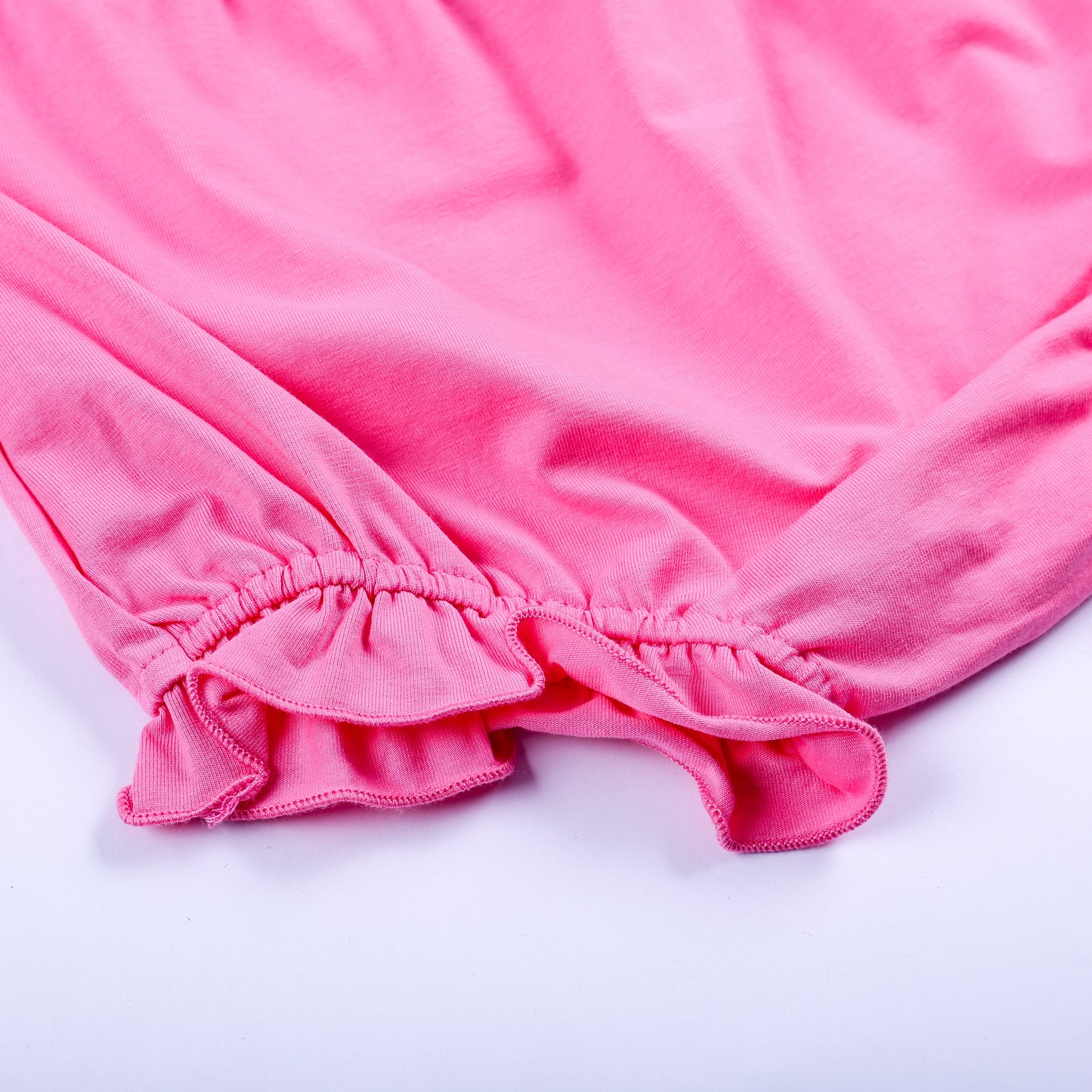 Close up view of elastic ruffle hem detail on solid pink diaper cover bloomer matching Big Sister set.