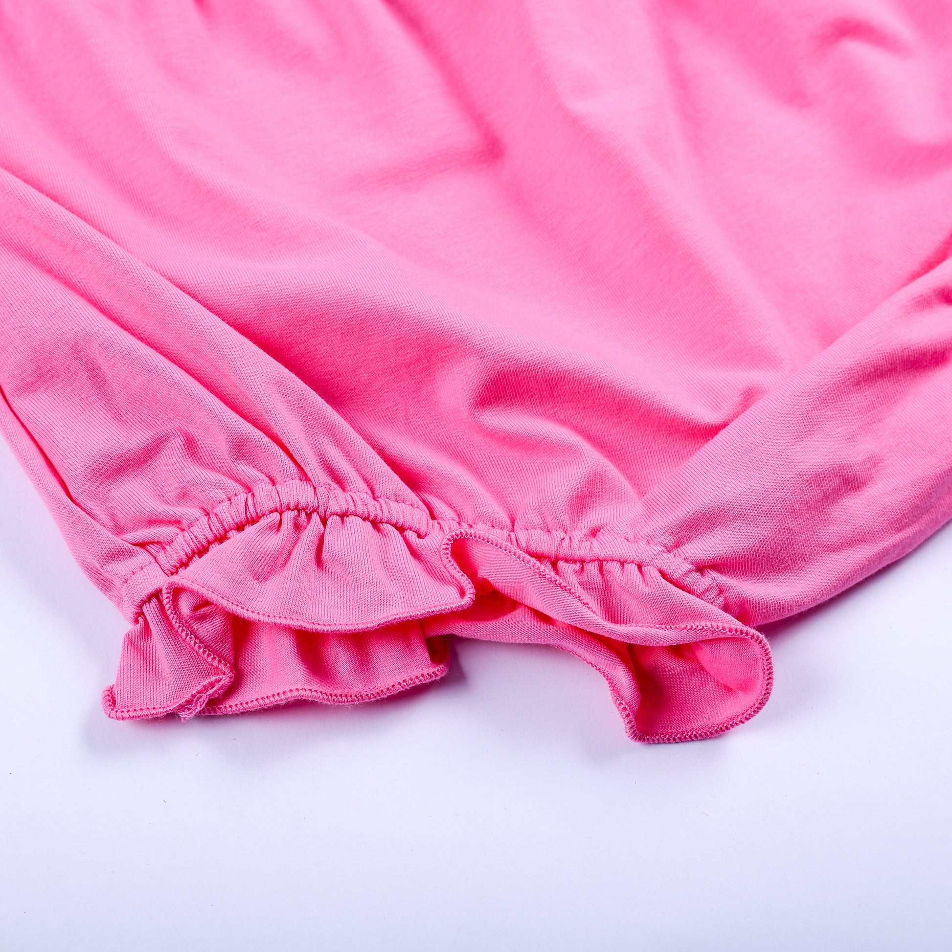 Close up view of elastic ruffle hem detail on solid pink diaper cover bloomer matching Big Sister set.