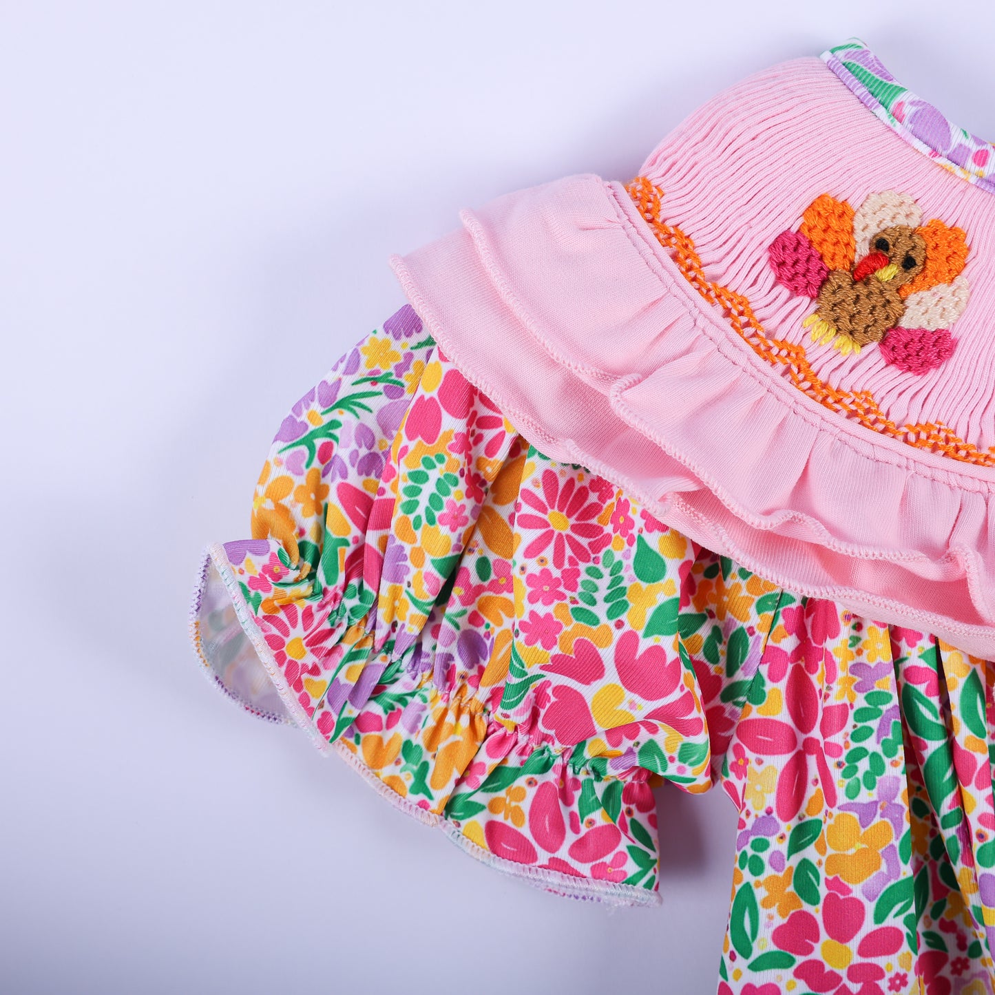 Close-up of the ruffled flutter sleeve and pink smocked collar with an embroidered turkey on the baby bubble romper.