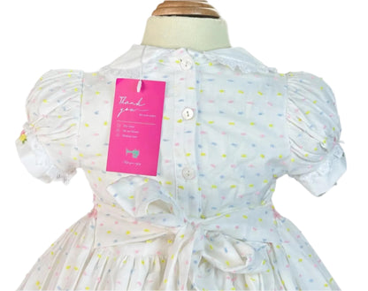 Back view of girls white smocked dress featuring hand embroidered pink flower basket and polka dot fabric with bow sash.