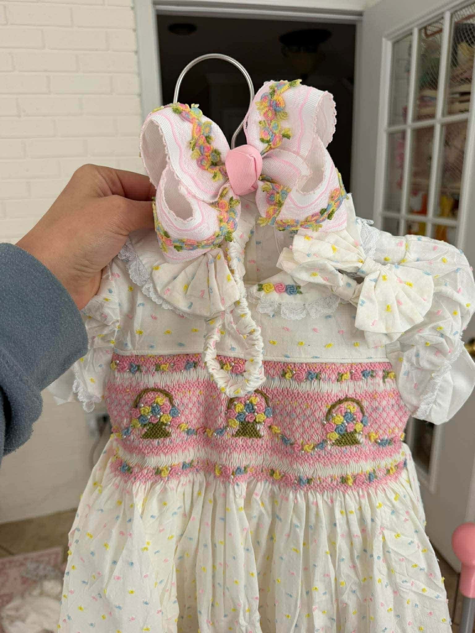 Child's dress with floral details and a hand holding it up.