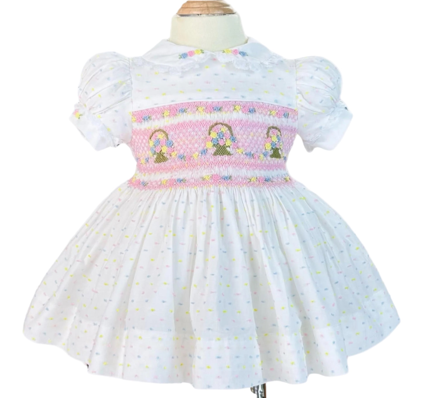 White dress featuring pink hand smocking with embroidered flower baskets and puff sleeves.