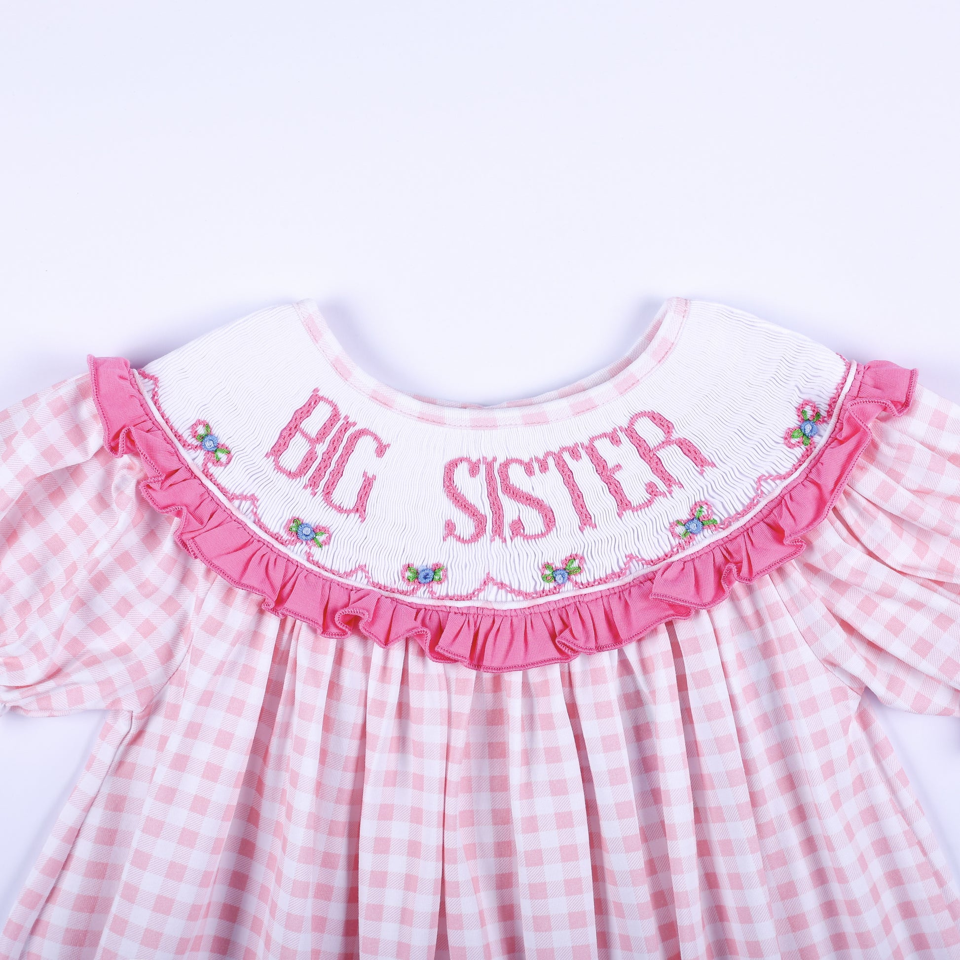 Close-up of hand-smocked white collar with pink Big Sister embroidery and floral accents on a gingham dress.