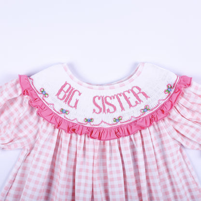 Close-up of hand-smocked white collar with pink Big Sister embroidery and floral accents on a gingham dress.