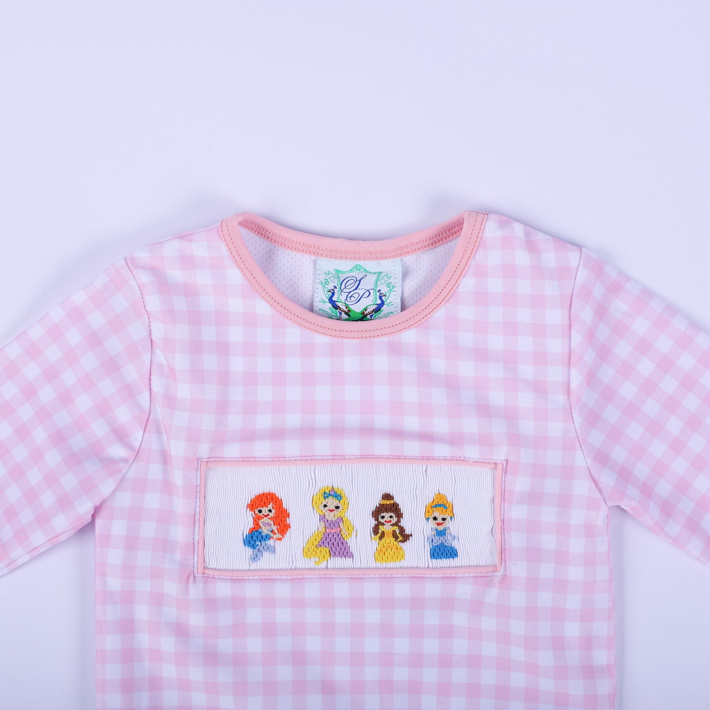 Close up of the girls pink gingham rash guard top neckline and hand smocked fairytale princess bodice embroidery.
