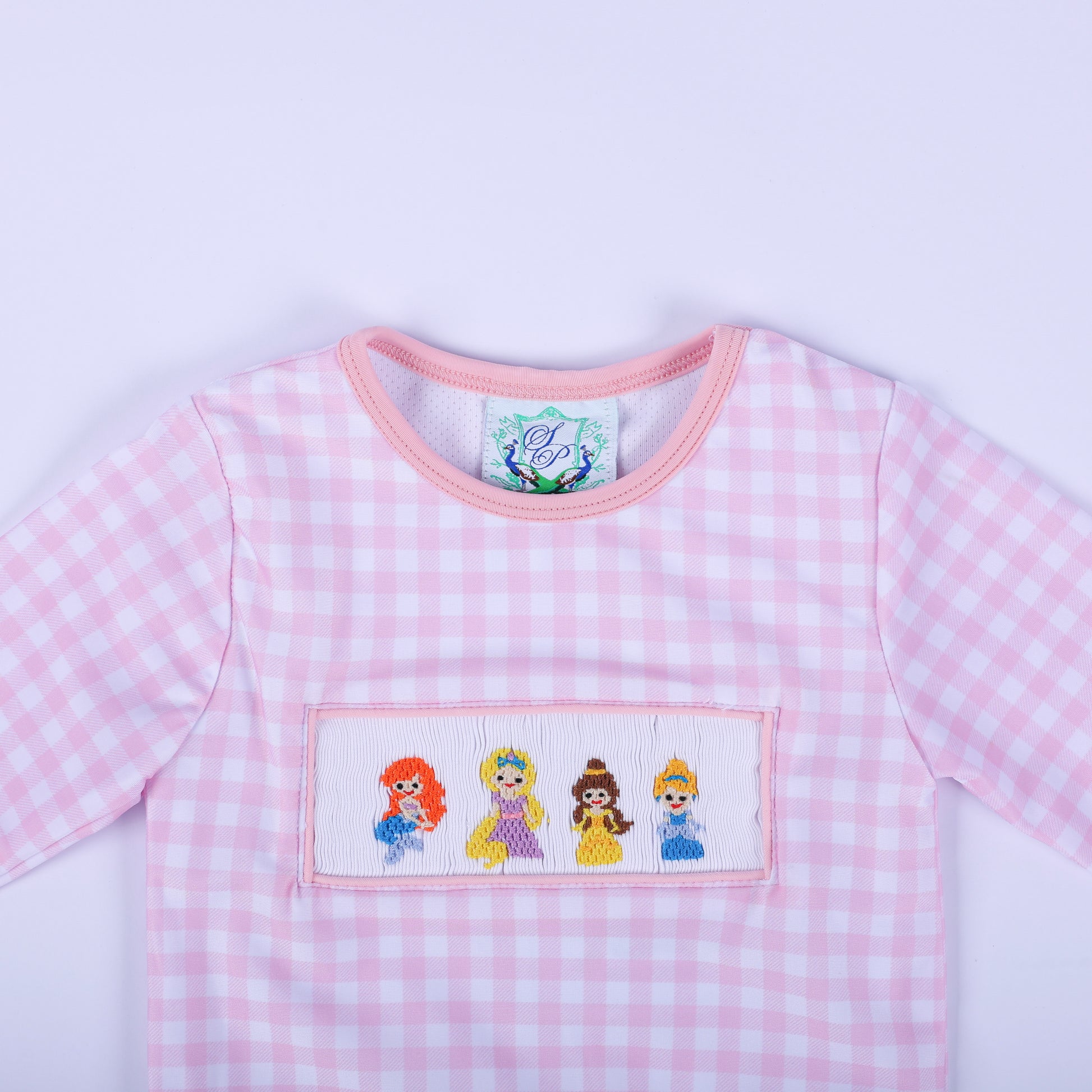 Close up of the girls pink gingham rash guard top neckline and hand smocked fairytale princess bodice embroidery.