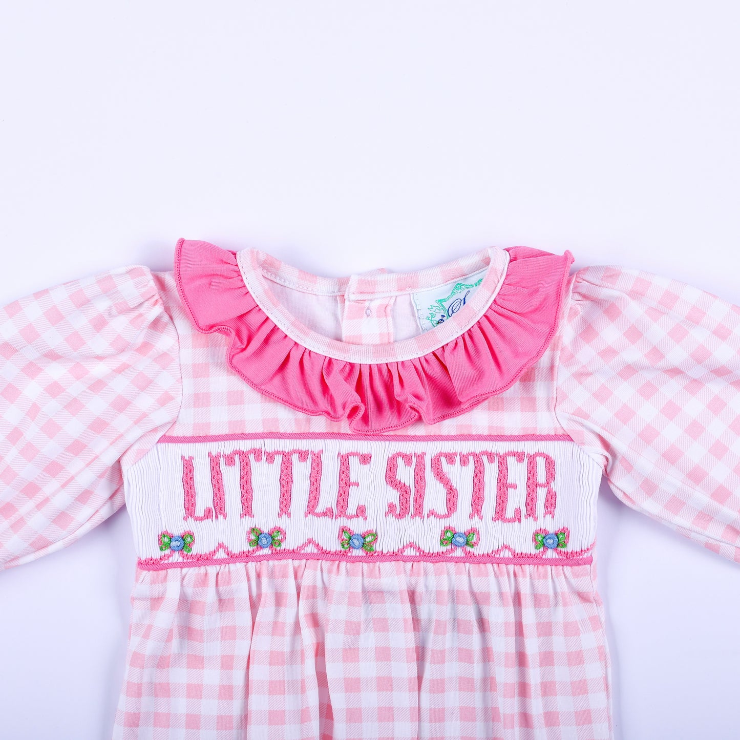 Close-up of pink gingham layette sleep sack showing hand embroidered Little Sister text and smocked bodice detail.