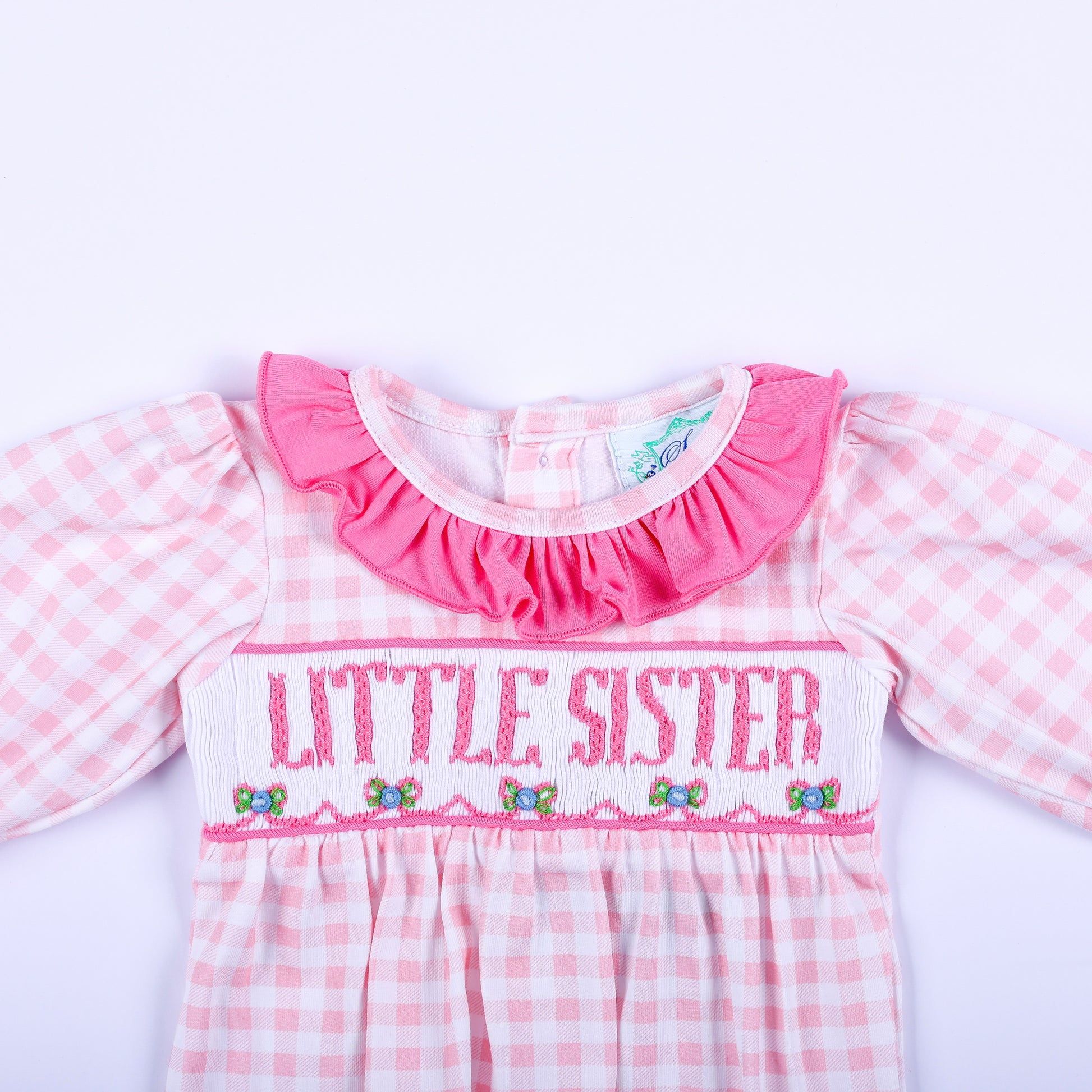 Close-up of pink gingham layette sleep sack showing hand embroidered Little Sister text and smocked bodice detail.