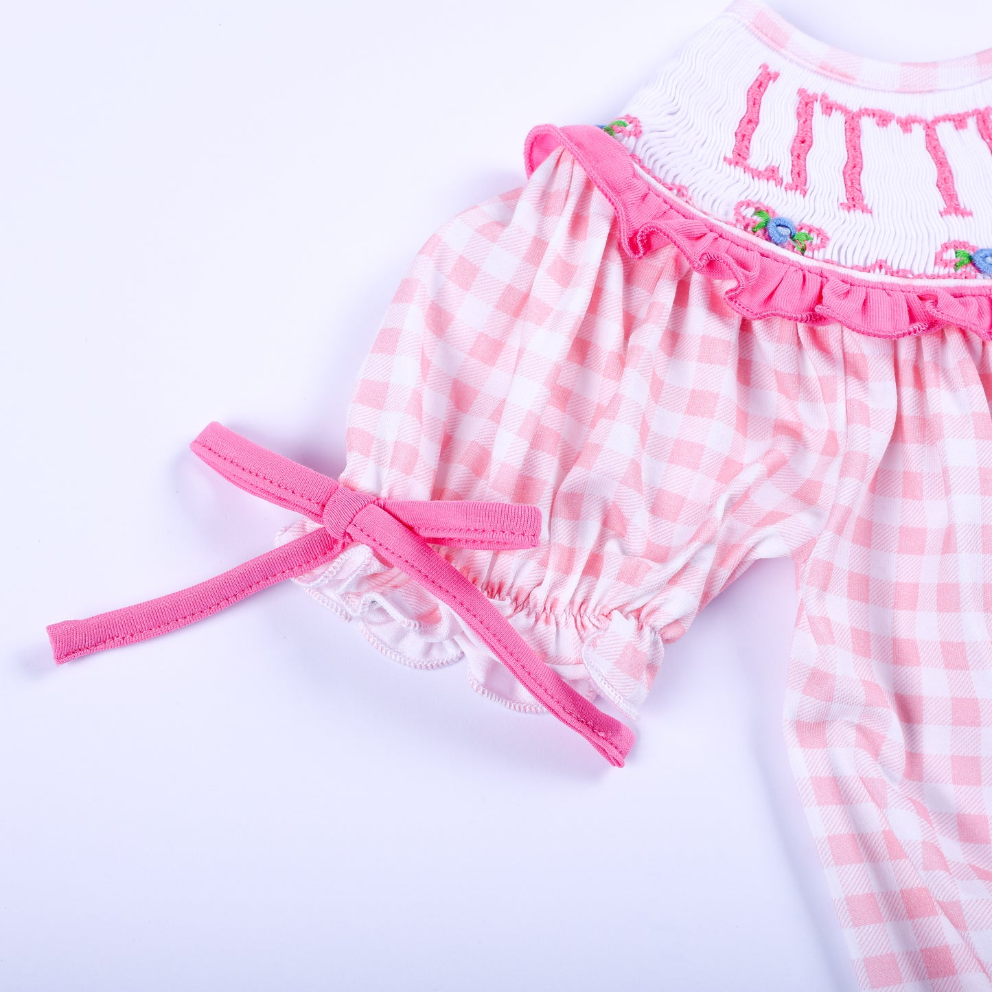 Detailed view of puffed short sleeve with pink bow tie on a pink gingham hand smocked Little Sister bubble outfit.