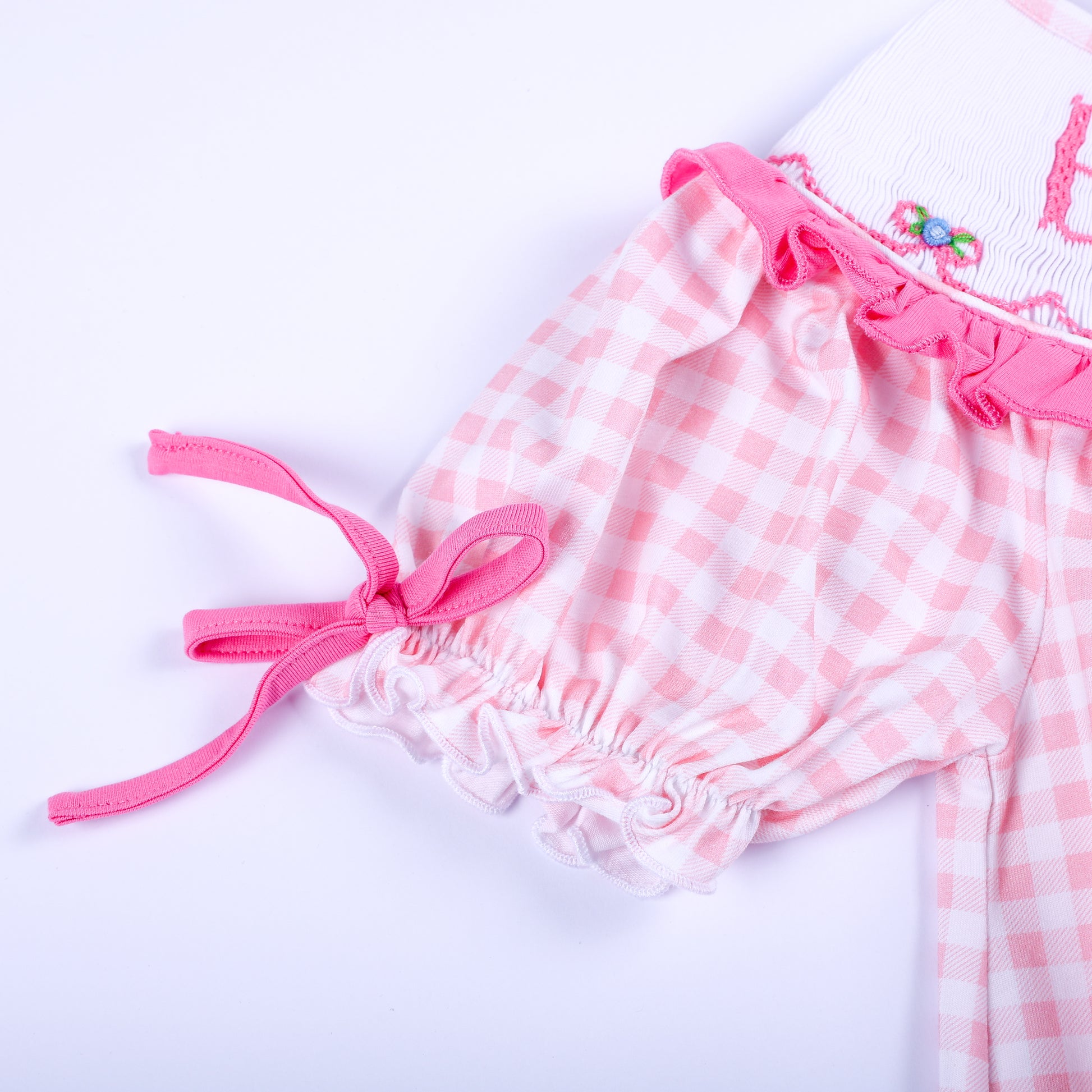 Detailed view of the puff sleeve with pink tie bow trim on a pink gingham Big Sister hand-smocked girl dress.