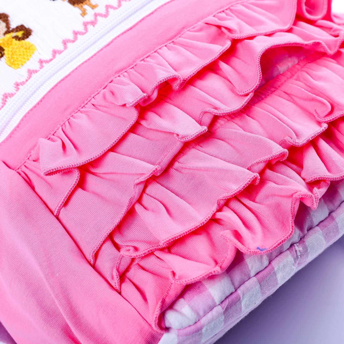 Close-up of layered pink fabric ruffles on front pocket of smocked fairytale princess backpack for girls.