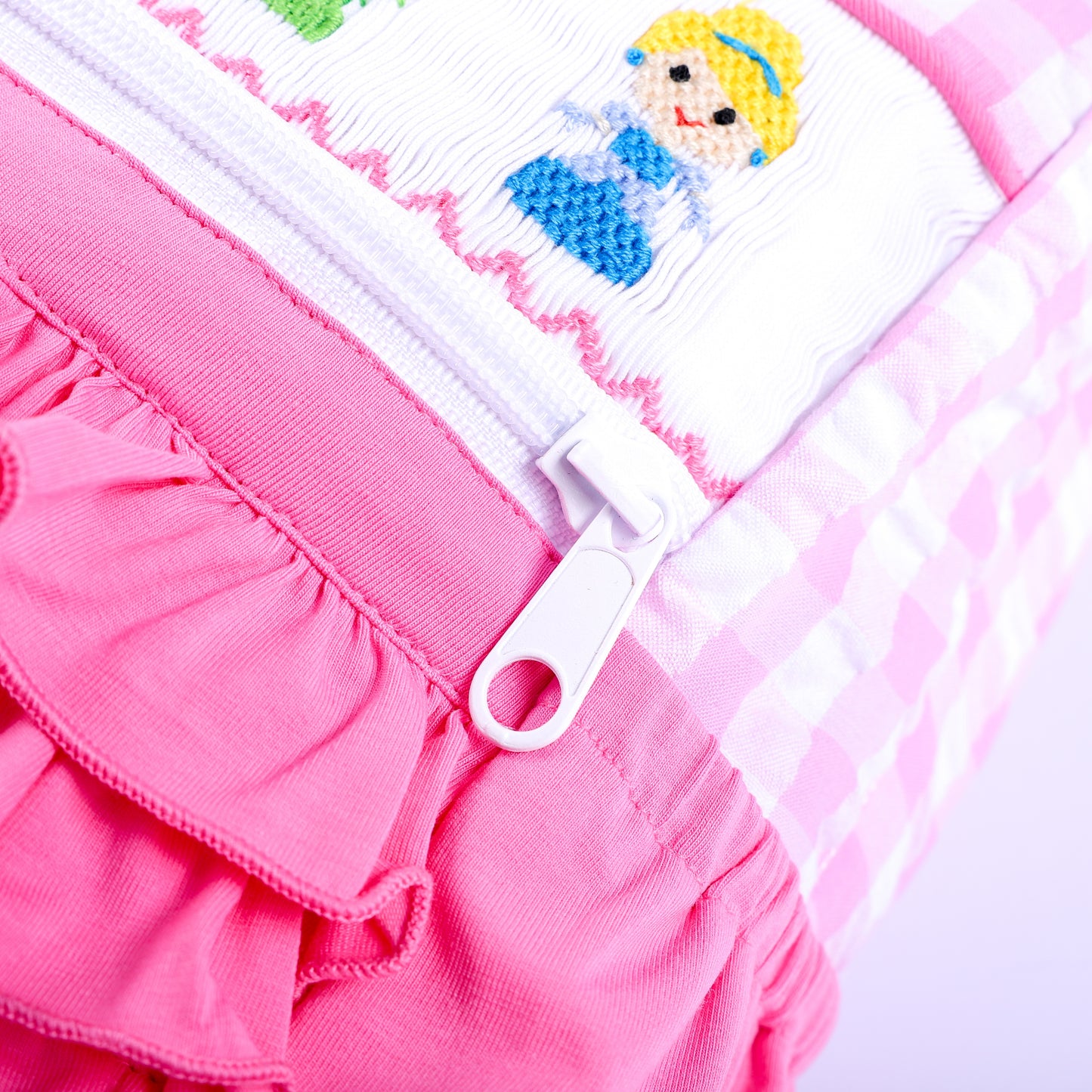Close-up view of sturdy zipper pull on a pink gingham hand-smocked fairytale princess backpack for kids.