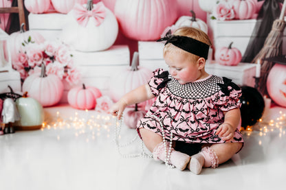 Baby girl sitting on floor in pink hand smocked bats bloomer set playing with pearls amidst fairy lights.