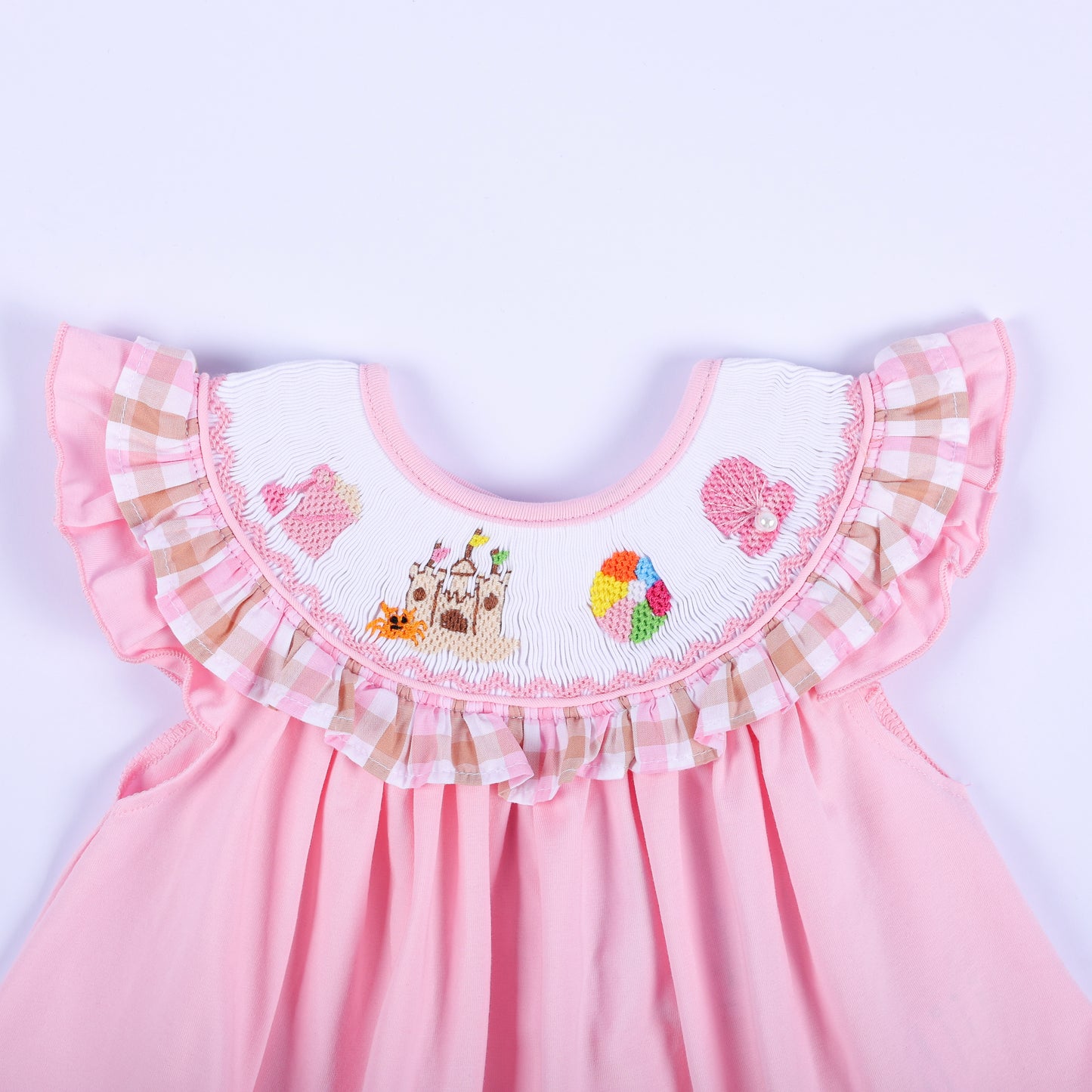 Close-up of hand embroidered beach scene yoke with sandcastle and beach ball on a pink smocked baby girl top.