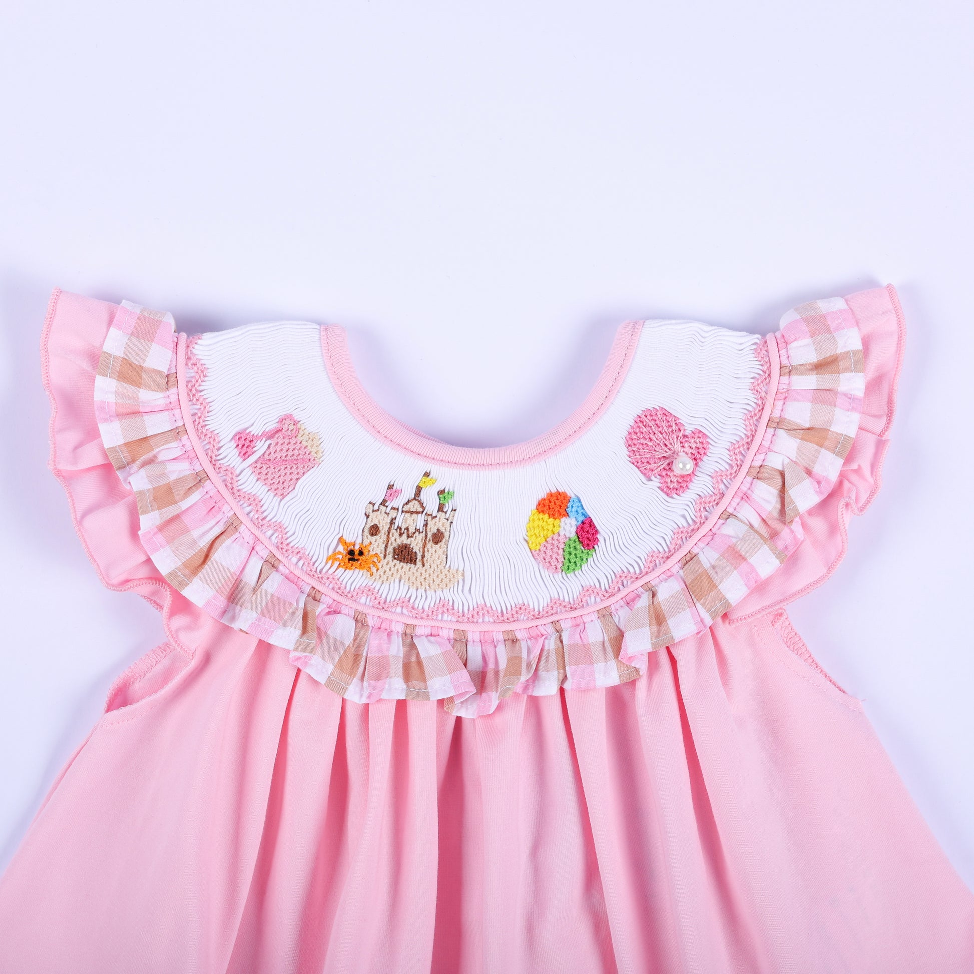 Close-up of hand embroidered beach scene yoke with sandcastle and beach ball on a pink smocked baby girl top.