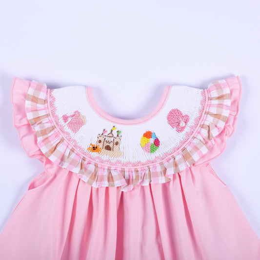 Close-up of hand embroidered beach scene yoke with sandcastle and beach ball on a pink smocked baby girl top.