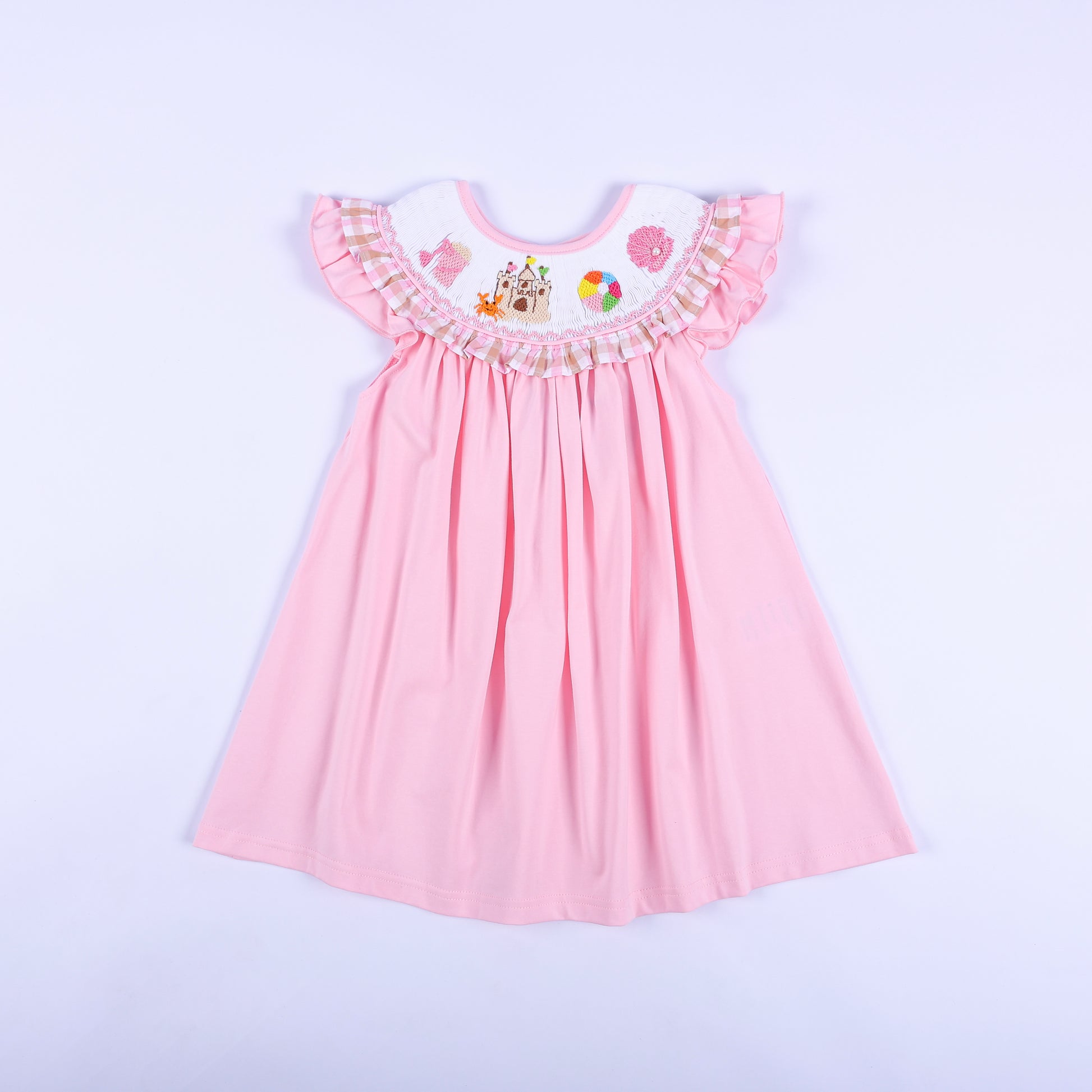 Pink hand smocked beach dress for girls with hand embroidered sandcastle motifs and gingham ruffle sleeve trim.