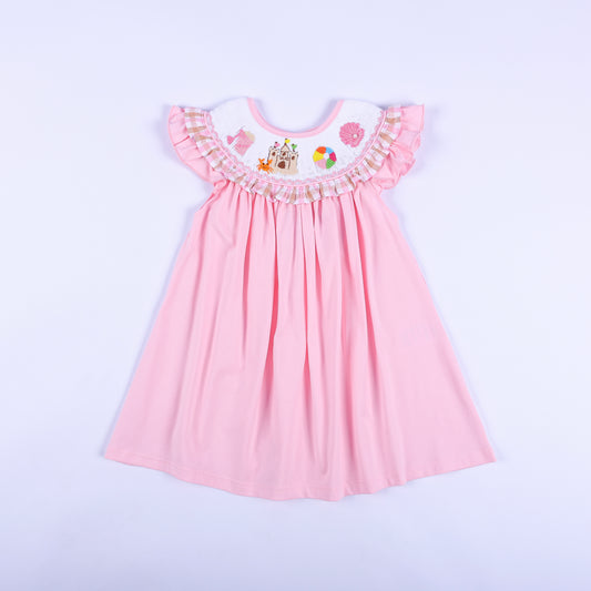 Pink hand smocked beach dress for girls with hand embroidered sandcastle motifs and gingham ruffle sleeve trim.