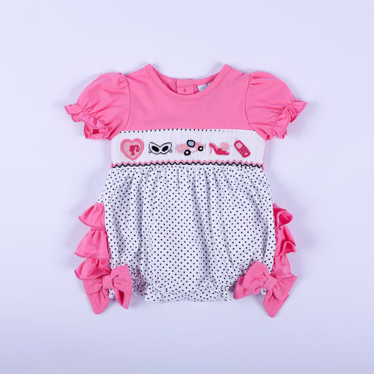 Pink polka dot hand-smocked baby girl bubble outfit featuring hand-embroidered fashion icons and ruffled sleeves.