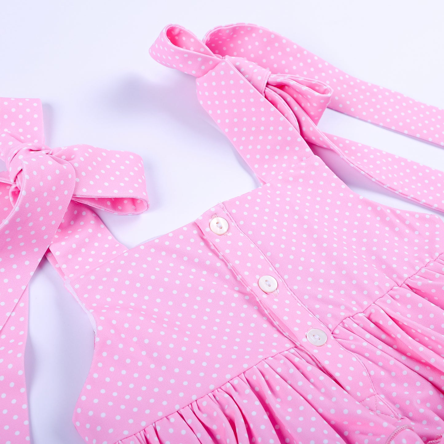 Detail shot of white button back closure and pink polka dot tie shoulder straps on boutique top.