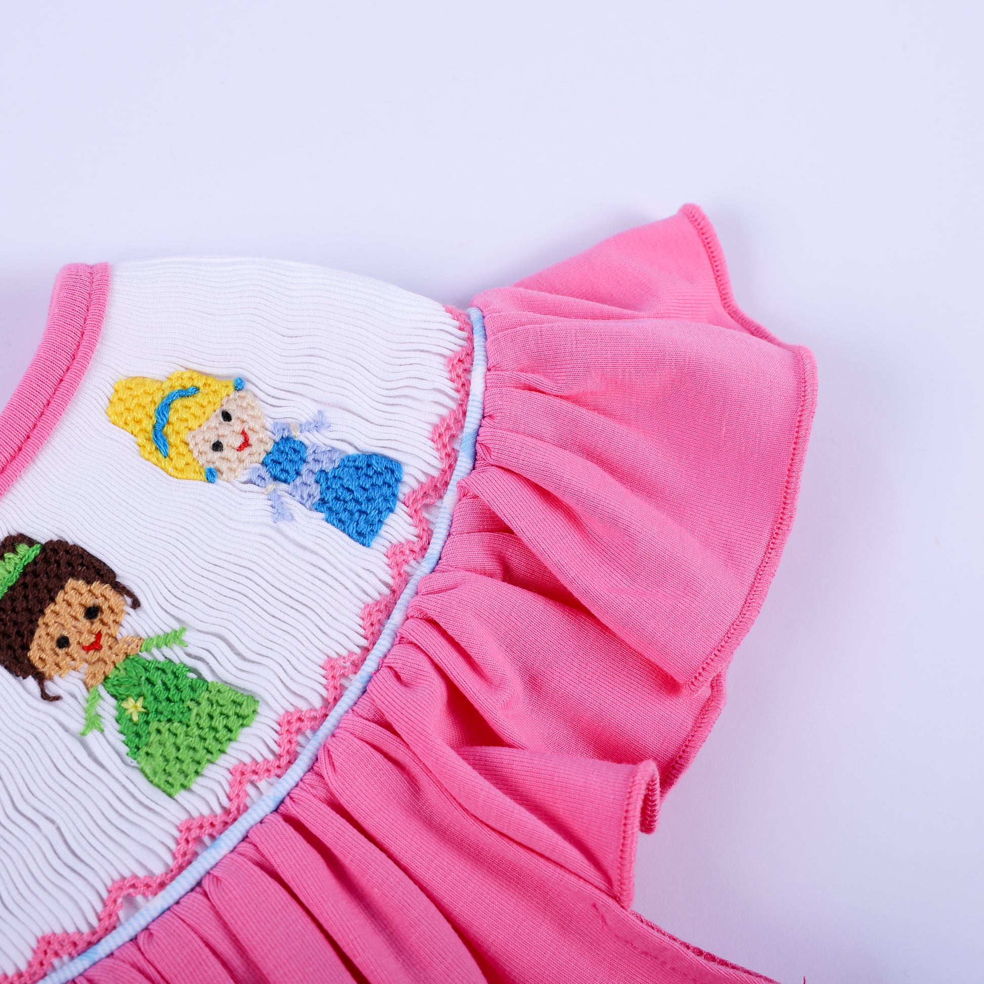 Detail view of flutter sleeve and delicate hand-embroidered princess smocking on a baby girl pink knit bubble outfit.