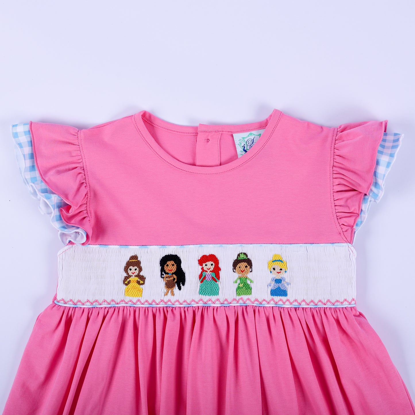 Bodice detail of pink princess knit hand smocked dress with embroidered princesses and blue gingham flutter sleeves.