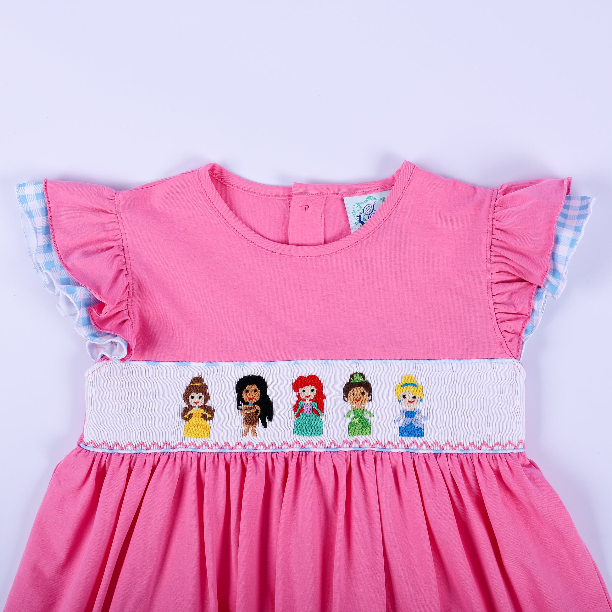 Bodice detail of pink princess knit hand smocked dress with embroidered princesses and blue gingham flutter sleeves.