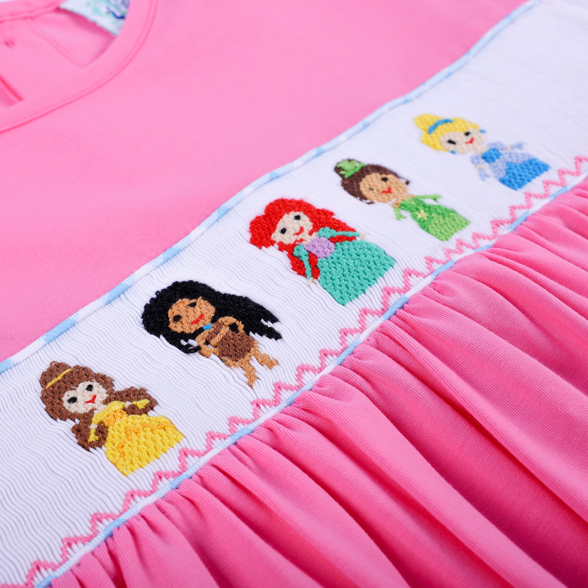 Angled close-up of hand smocked plate featuring hand embroidered princesses on pink knit dress with gathered skirt.