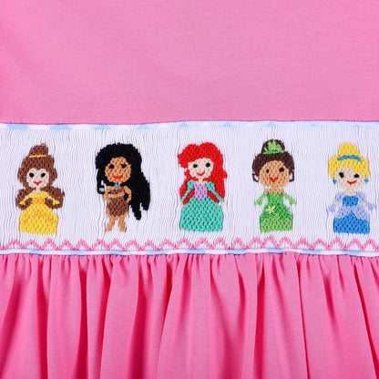 Angled close-up of intricate hand smocked band with hand embroidered princess figures on pink knit dress.