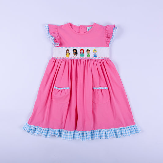 Full front view of girls pink princess knit hand smocked dress featuring blue gingham ruffle trim and pockets.
