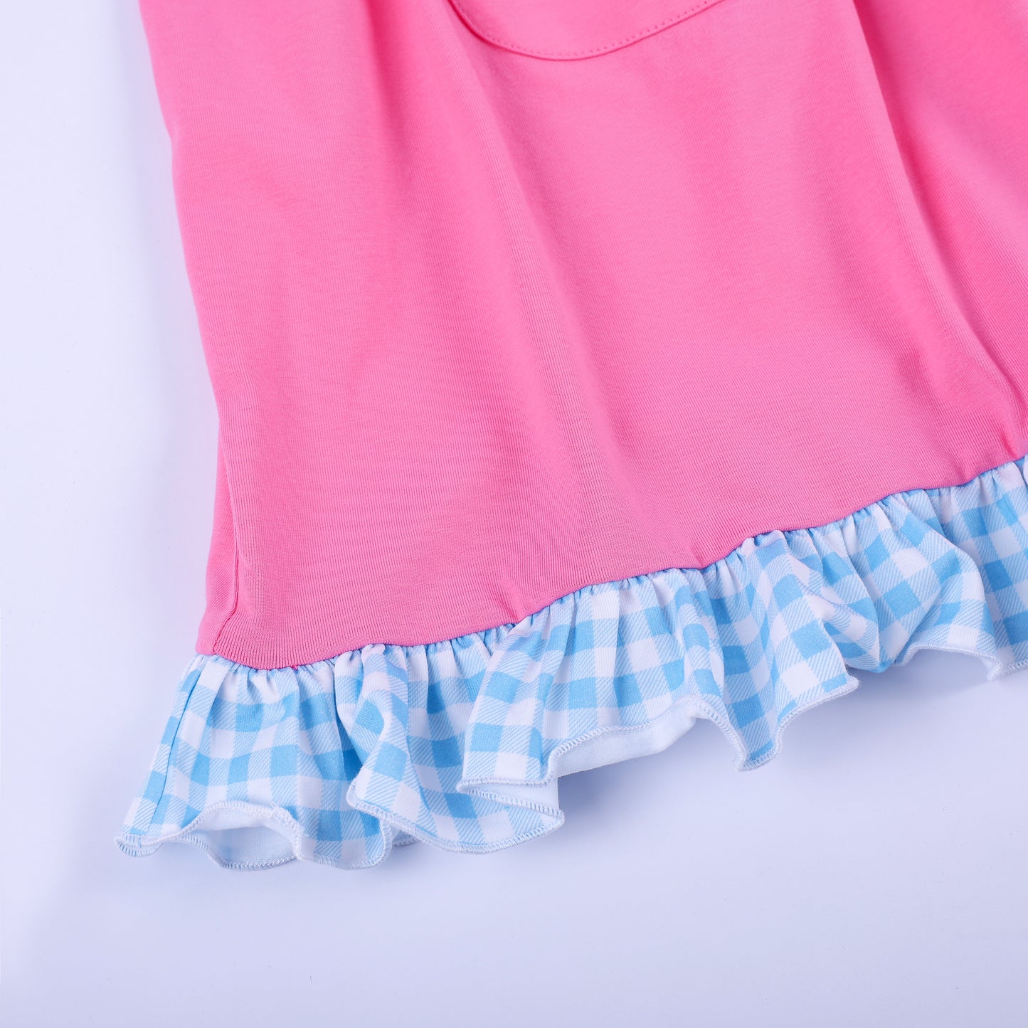 Close-up of bottom hem with blue gingham check ruffle trim on girls pink knit hand smocked princess dress.