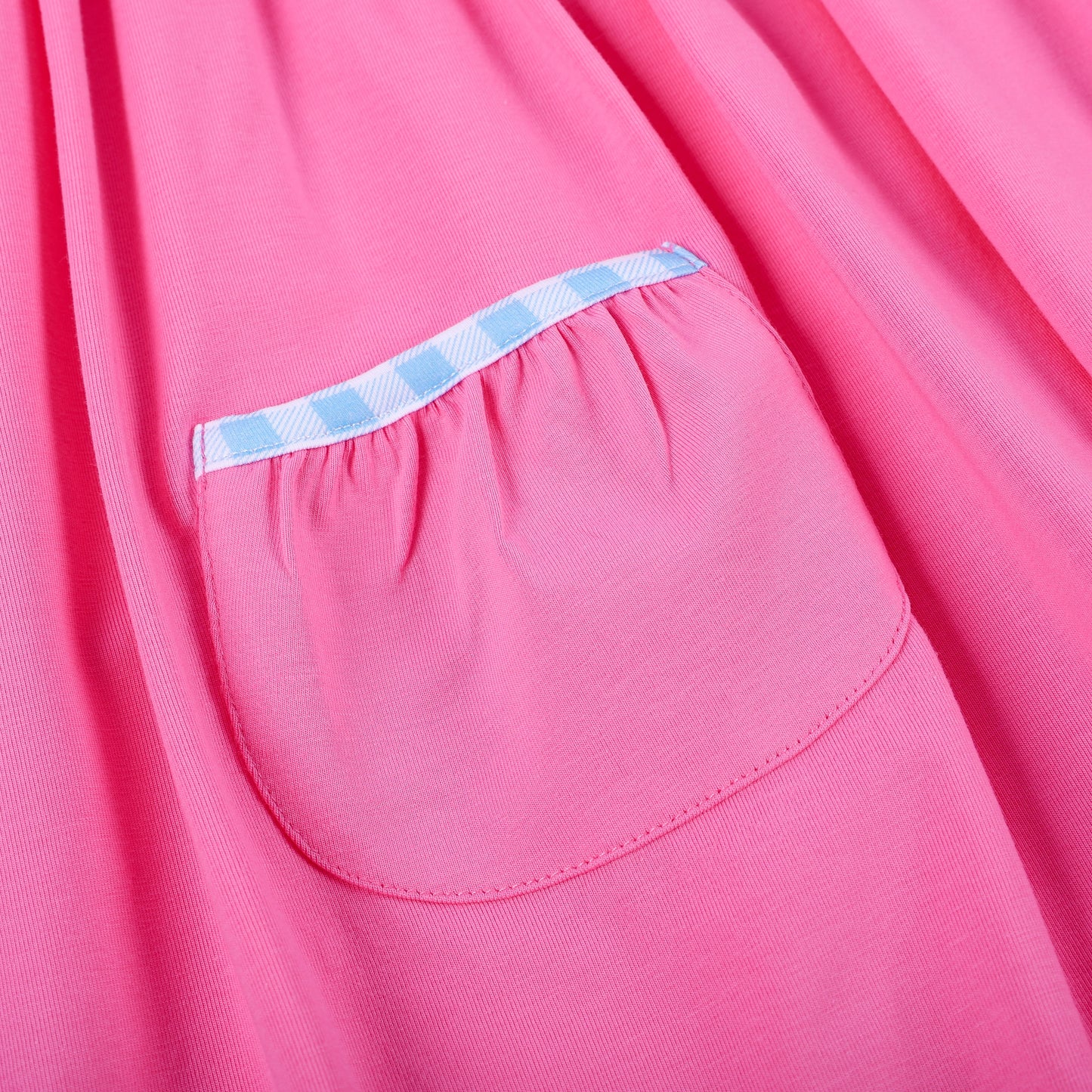 Detail of pink knit skirt pocket trimmed with blue gingham piping on hand smocked embroidered princess dress.