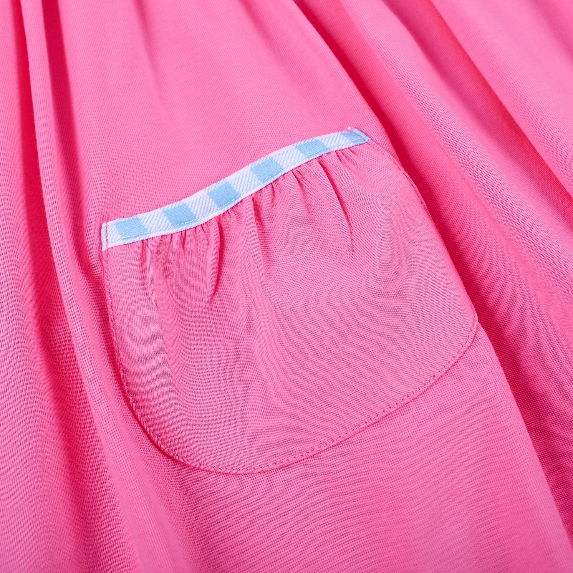 Detail of pink knit skirt pocket trimmed with blue gingham piping on hand smocked embroidered princess dress.