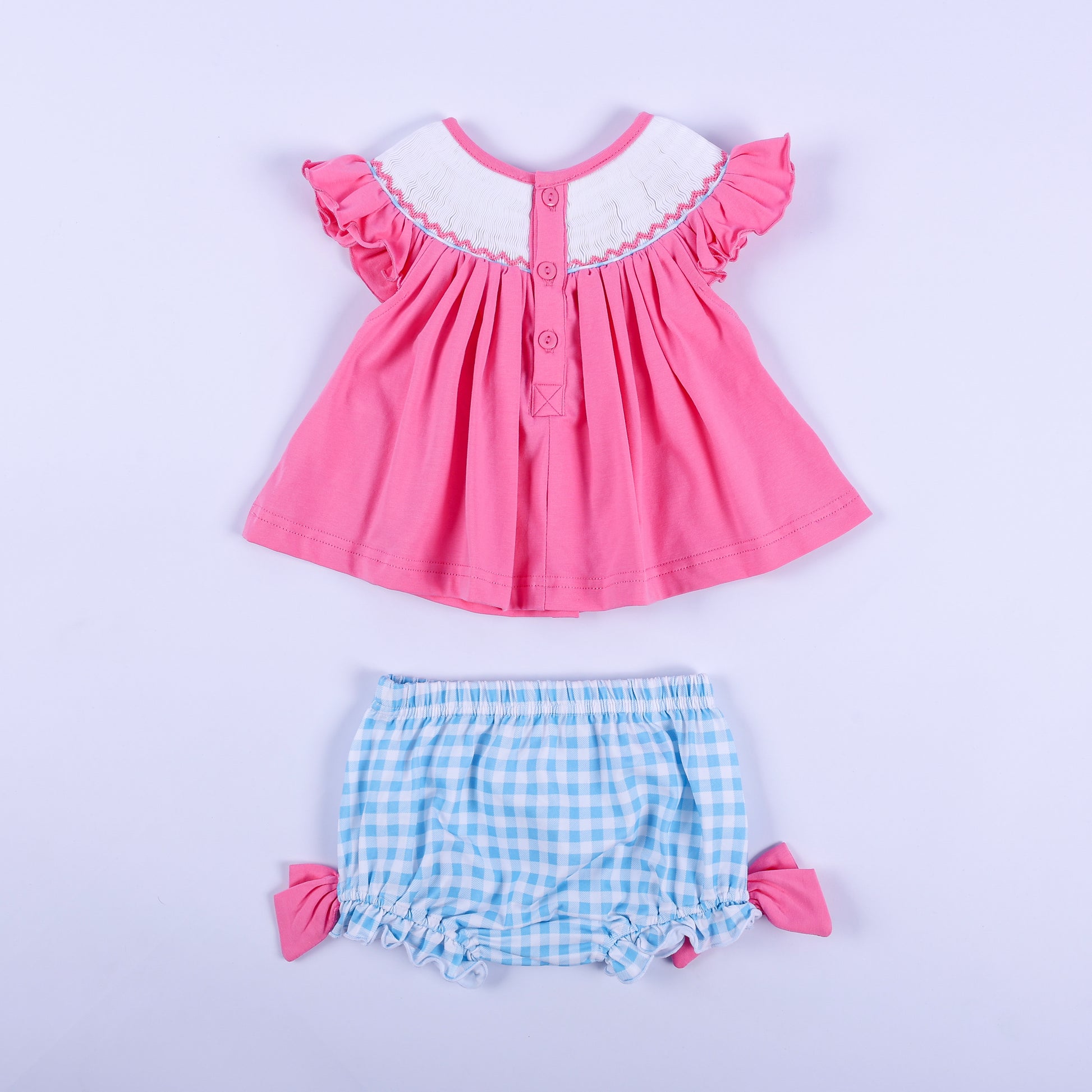 Back view of pink knit hand-smocked top with button closure and blue gingham bloomer set for baby girls.